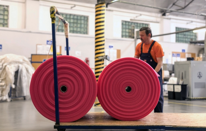 two rolls of pink film on a cart behind a man with a mustache working in a warehouse